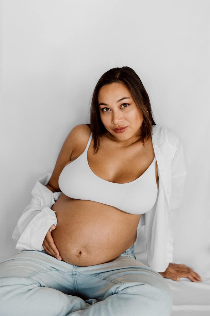 Schwangere Frau sitzt am Boden und hält ihren Bauch.