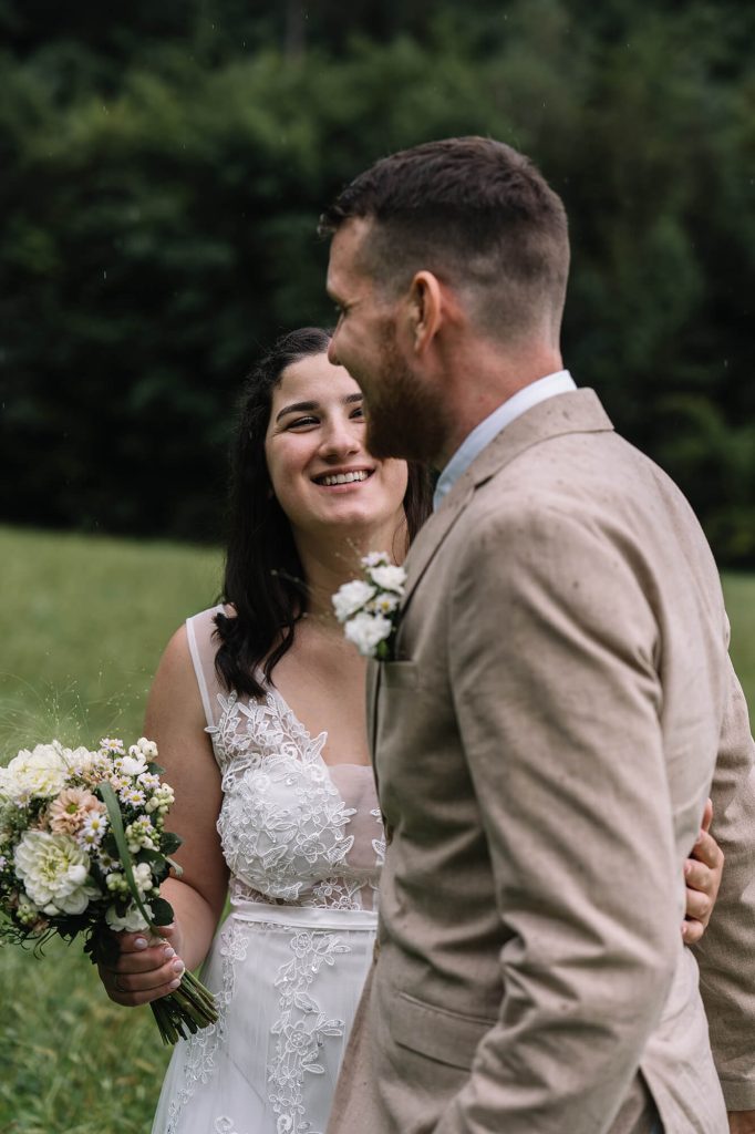Brautpaar steht auf einer Wiese und lächelt sich an.